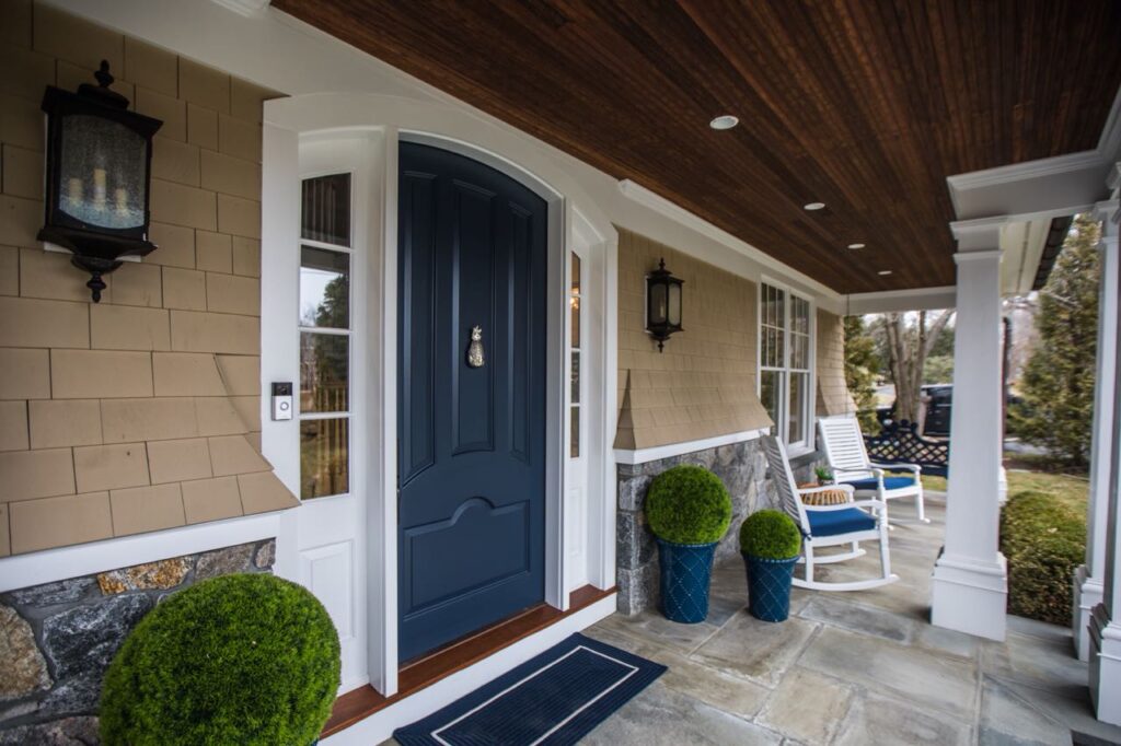 Covered front porch with a navy blue front door, cedar shingle siding, black lanterns and white rocking chairs