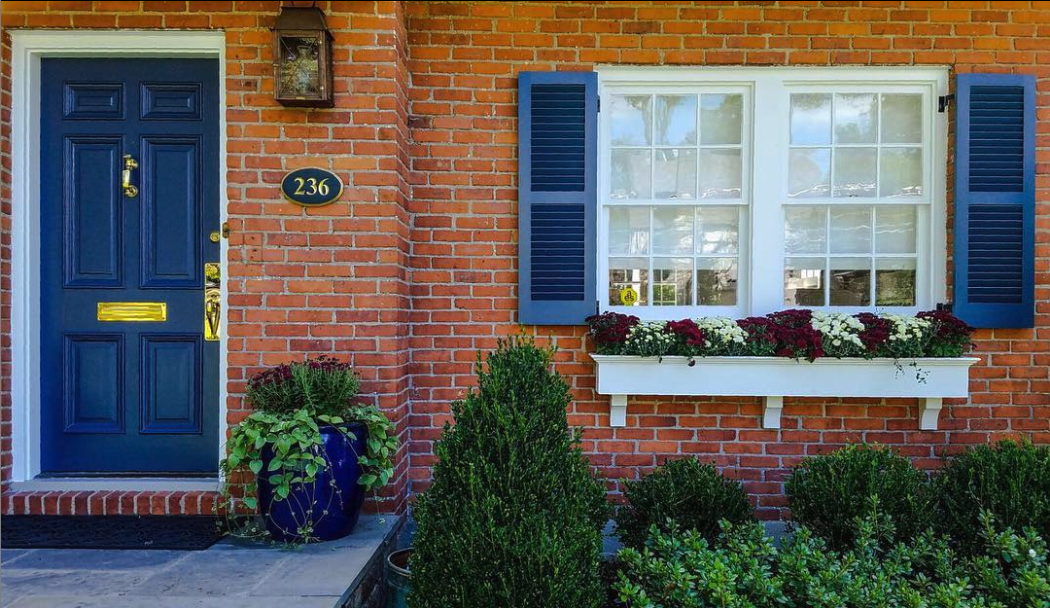 Red brick house with a navy front door, navy shutters and a white window box full of flowers