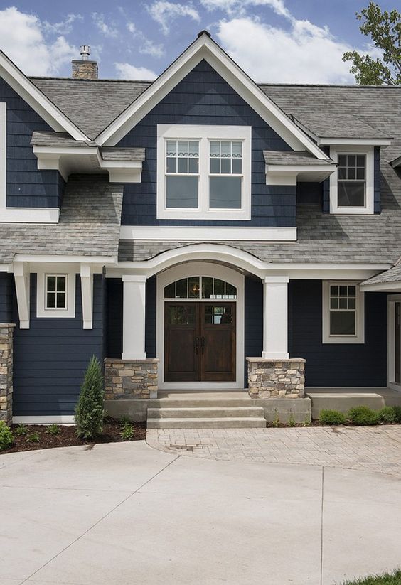 Navy blue house with white trim, an arched entry, stone column bases and dark wood double doors