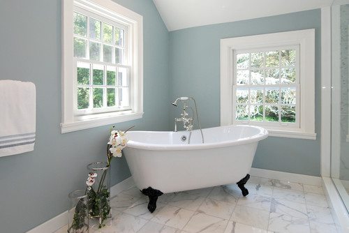 Bathroom with pale blue-gray walls, a white clawfoot tub with black feet, a marble floor and two white windows