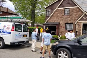 Painters gathered outside a brick house next to a white work van with ladders on its roof