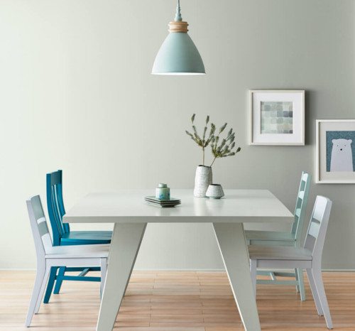 Dining area with pale gray-green walls, a white table, white and teal chairs and a pale blue pendant light