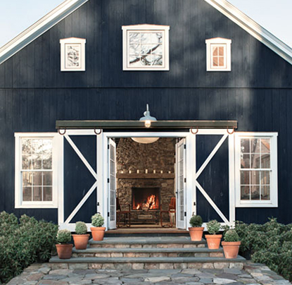 Navy board and batten barn house with white trim and open sliding doors showing a stone fireplace