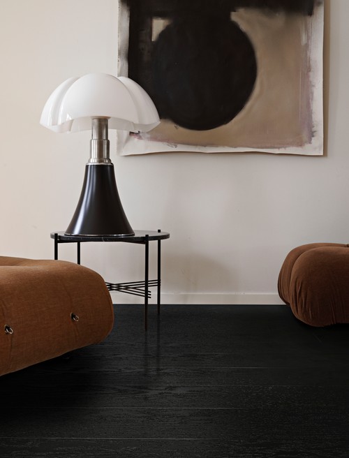 Living room with a black wood floor, a mushroom table lamp, a round side table and abstract art on a white wall
