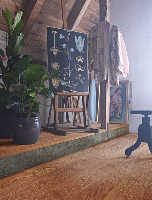 Attic room with a golden oak floor, exposed wood beams, a botanical chart on an easel and potted plants