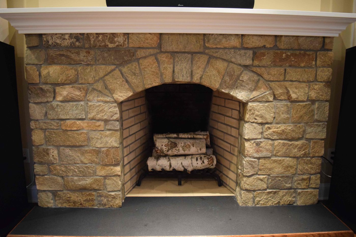 Stone fireplace with an arched opening, a brick-lined firebox, birch logs and a white mantel