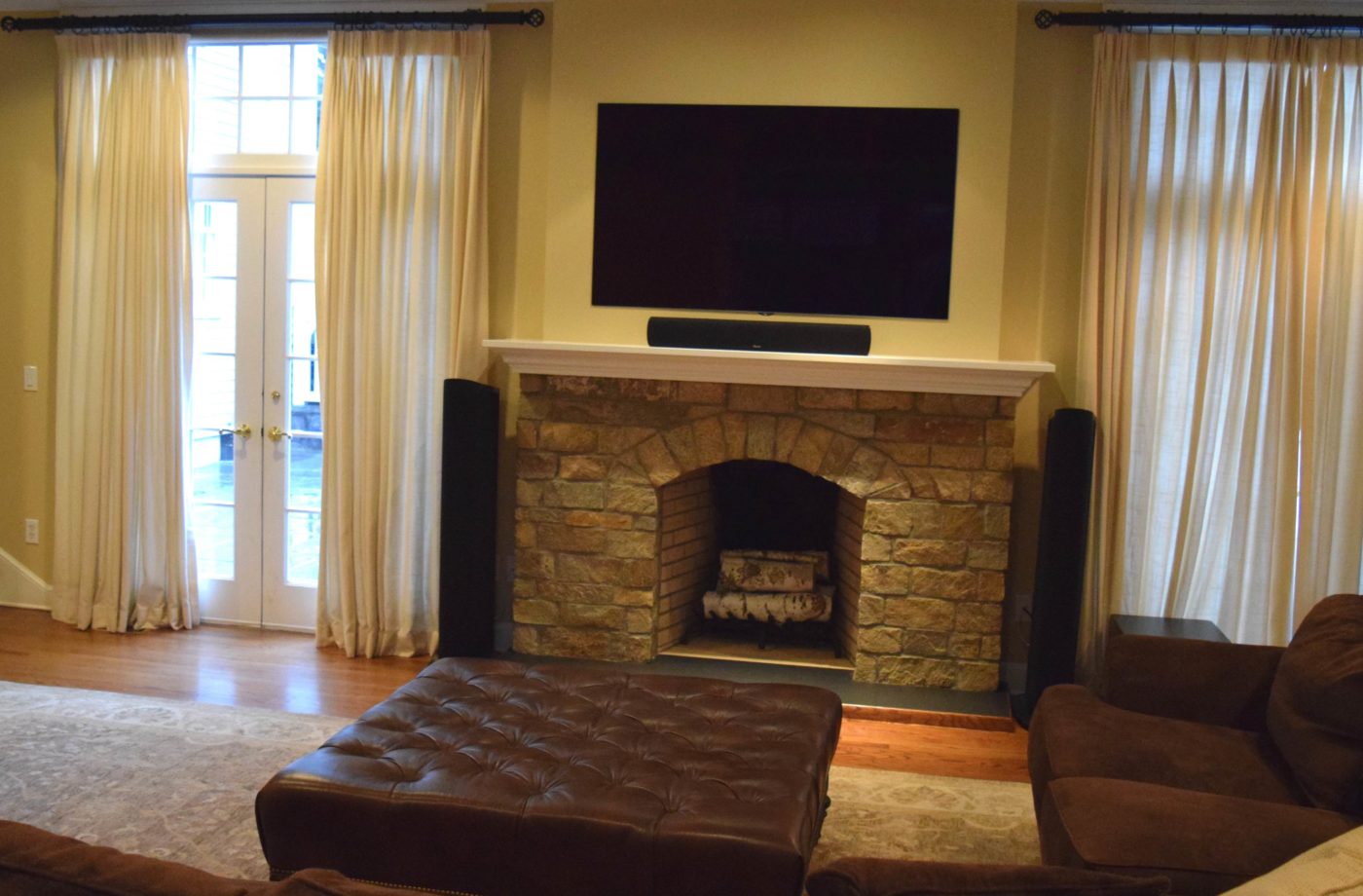 Family room with an arched stone fireplace, a TV above the white mantel, French doors and a tufted leather ottoman