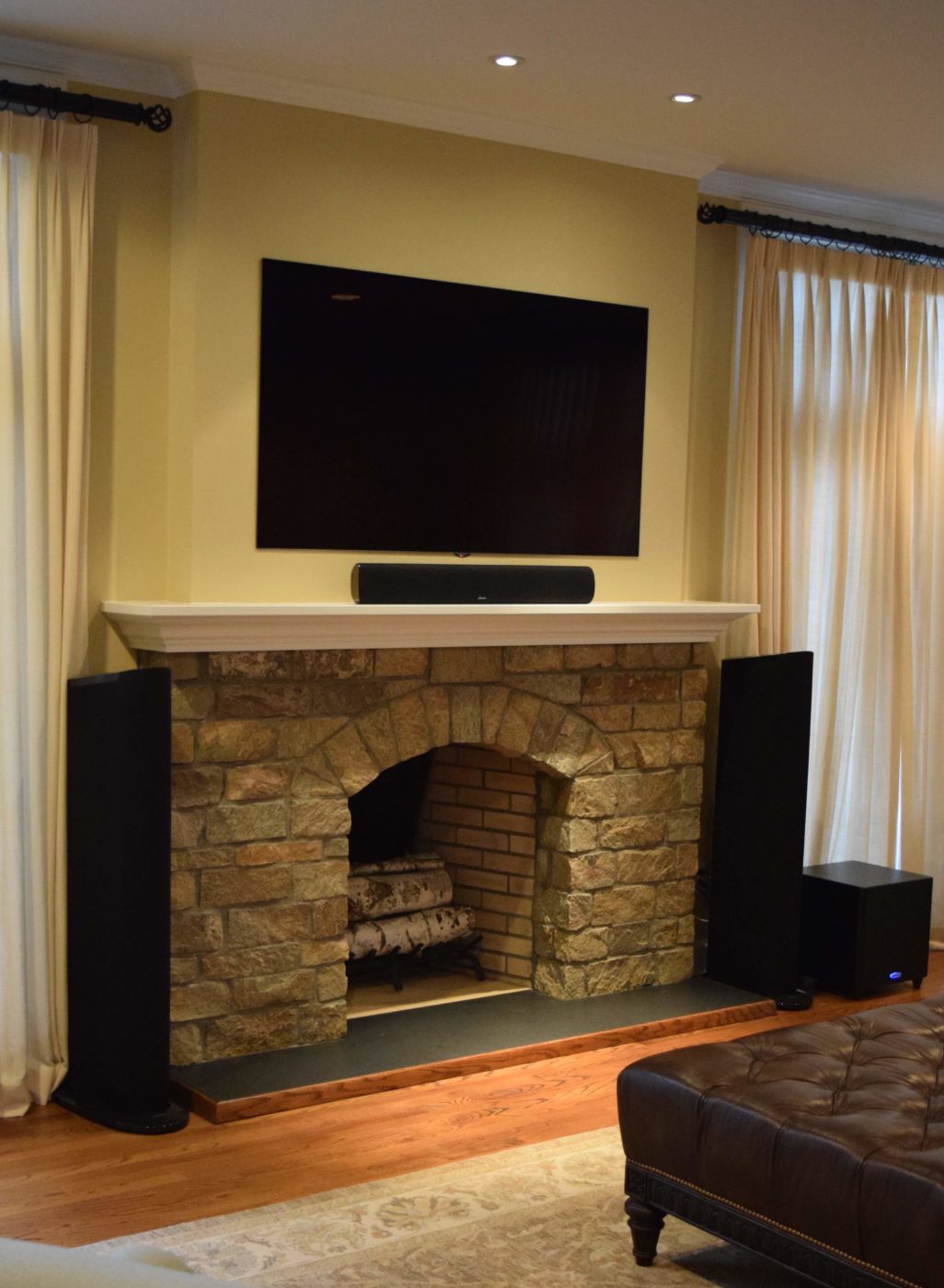 Stone fireplace with a white mantel, a wall-mounted TV above and tall speakers on each side
