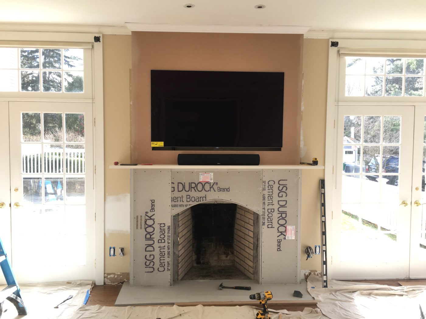 Fireplace mid-renovation with cement board around the arched firebox, a TV mounted above and drop cloths on the floor