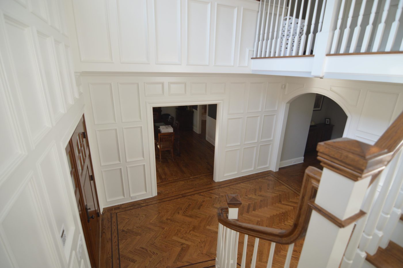 Two-story foyer with floor-to-ceiling white panel molding, a herringbone wood floor and a stair railing in front