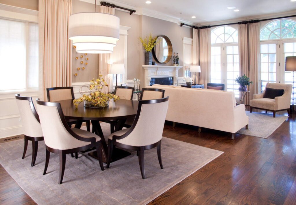 Open living and dining room with a round dark wood table, cream upholstered chairs, a drum pendant and a cream sofa