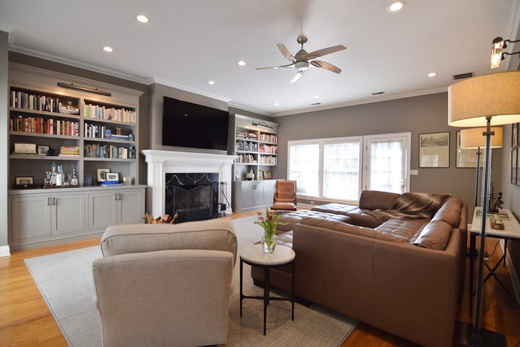 Family room with gray built-in bookshelves, a white fireplace mantel, a mounted TV and a brown leather sectional