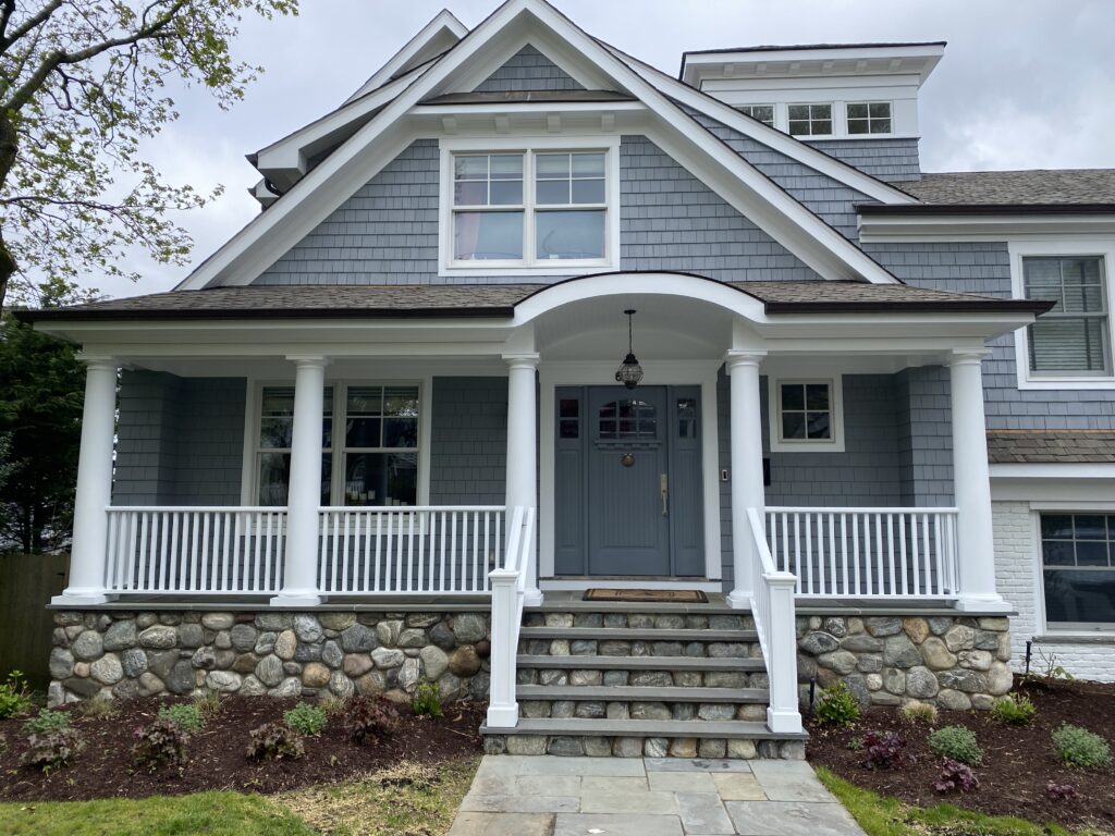 Blue-gray shingle siding and a white front porch with stone steps and a bluestone walk