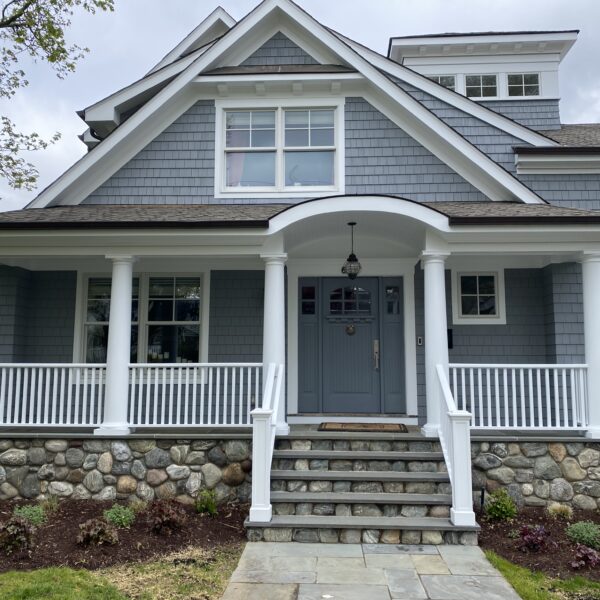 Blue-gray shingle siding and a white front porch with stone steps and a bluestone walk
