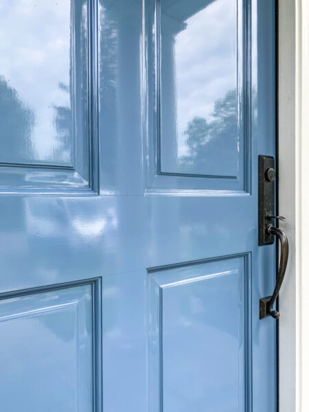 Close-up of a glossy light blue paneled door with a dark bronze handle and deadbolt