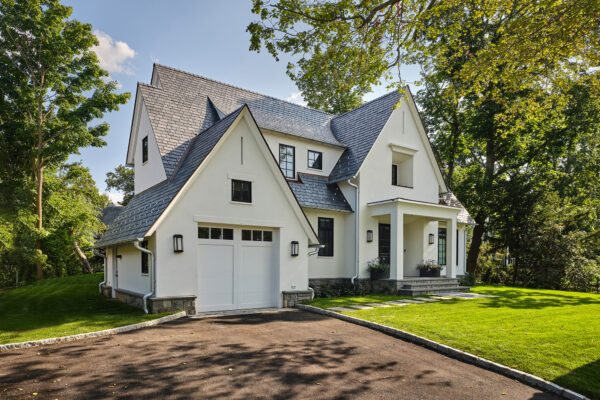 White two-story house with a steep gray shingle roof, attached garage, covered porch and paved driveway