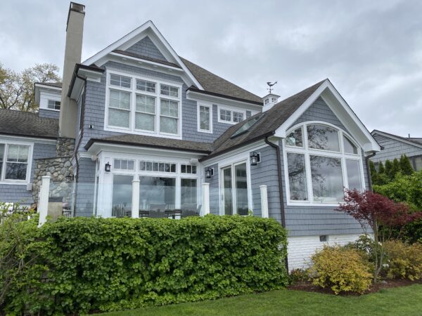 Two-story house with blue-gray siding, white trim and large windows behind a trimmed green hedge
