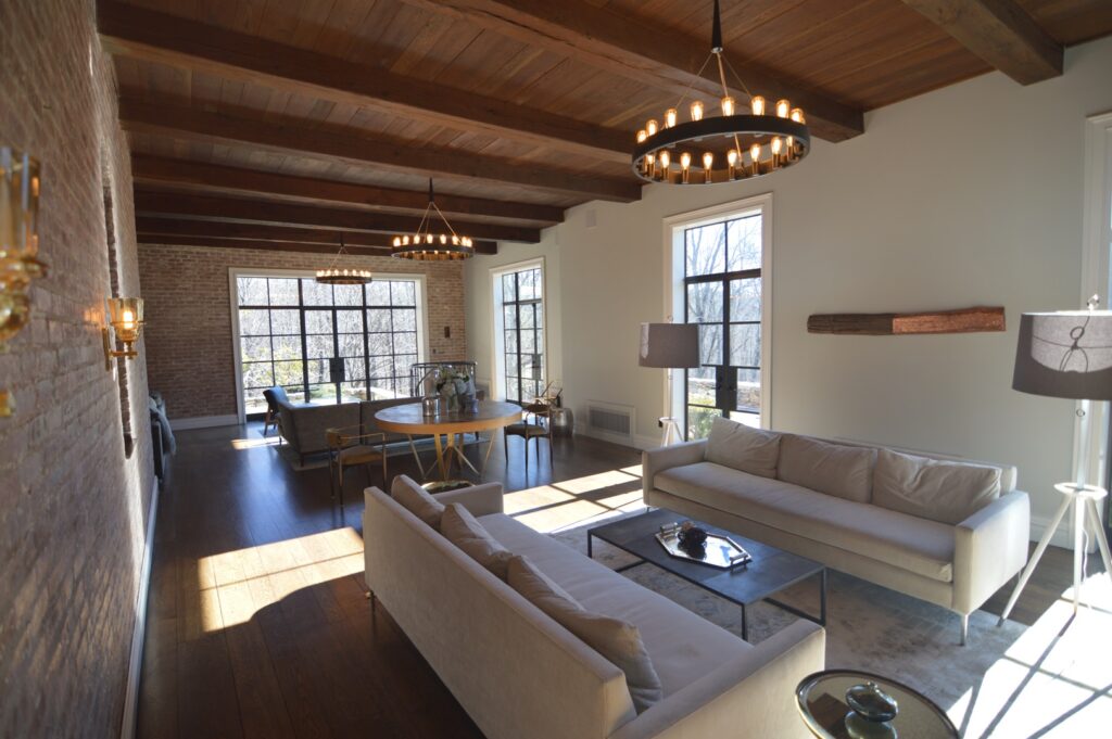Loft living room with an exposed brick wall, a dark wood beamed ceiling, ring chandeliers and cream sofas