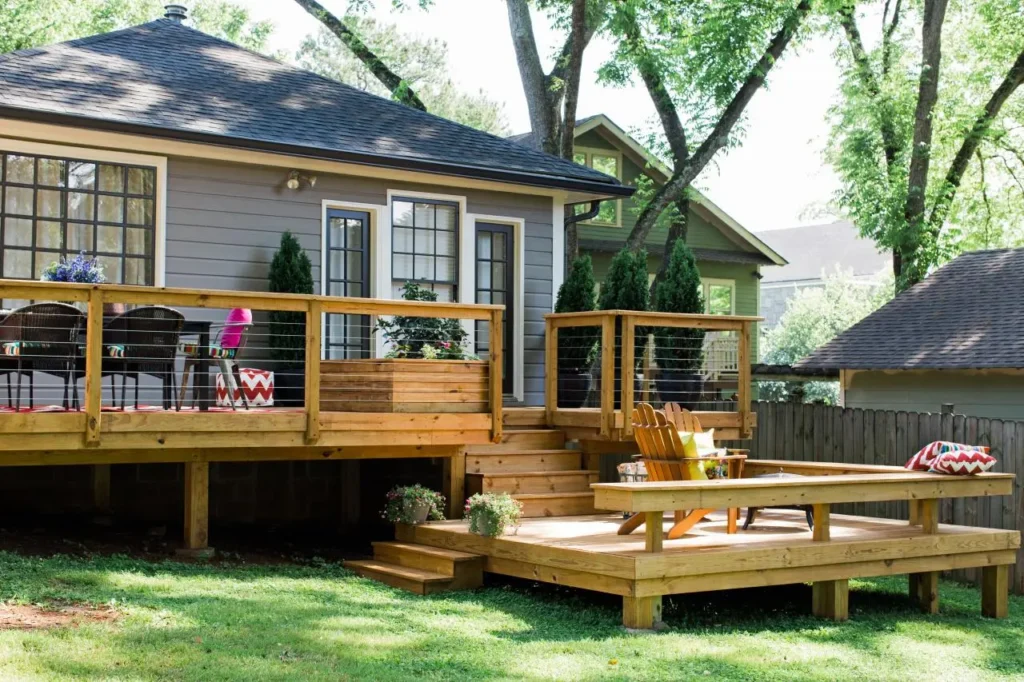 Two-level natural wood deck with cable railings, wide steps and an Adirondack chair behind a gray house