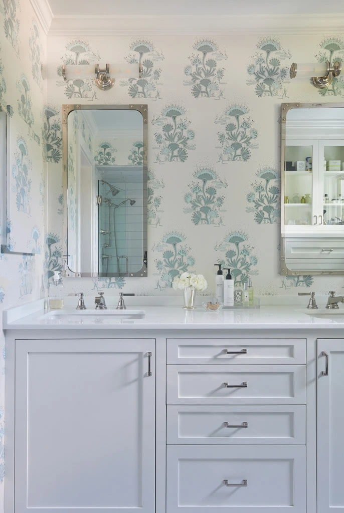 Bathroom with blue and green floral wallpaper, a white double vanity with a marble top and two mirrors