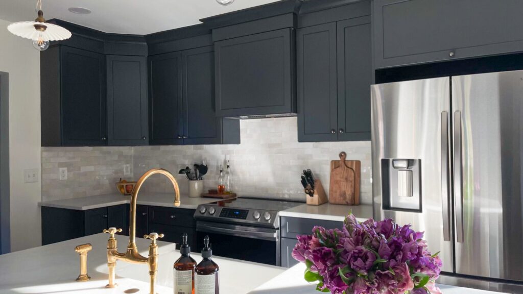 Kitchen with charcoal navy painted shaker cabinets, a white quartz counter and a brass bridge faucet