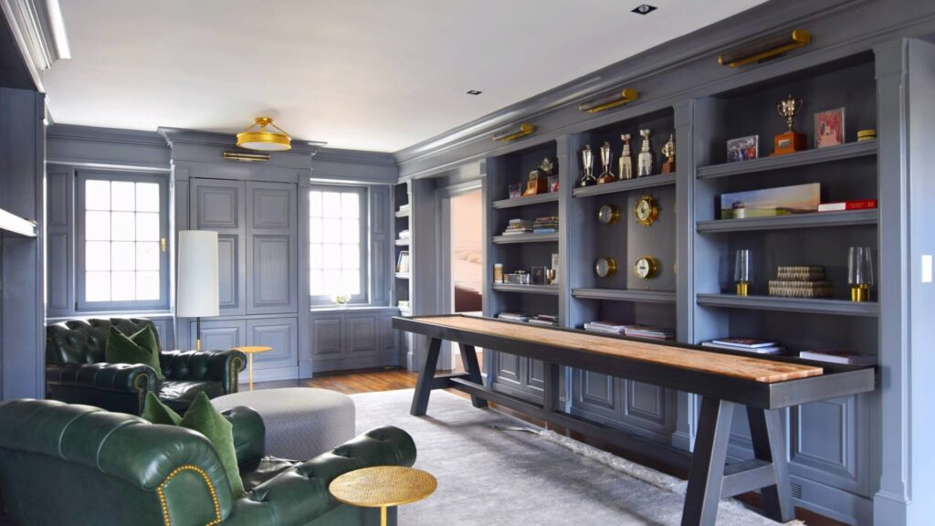 Library with gray blue painted built-in bookshelves, paneled walls and crown molding, a long wood table and green leather chairs